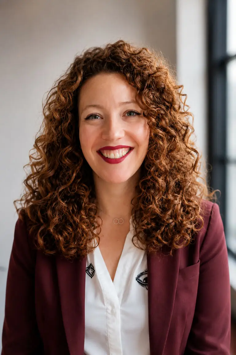 Portret van Naomi met krullend haar in bordeaux blazer en wit shirt bij daglicht